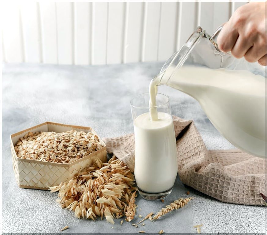 Oat grains and hand filling from a jug a glass with oat milk